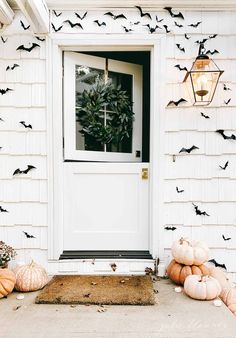 bats decorate the front door of a house with pumpkins on the ground and a lantern