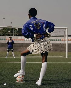 a woman standing on top of a soccer field next to a goalie wearing a skirt