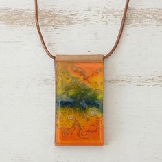 an orange, yellow and green pendant hangs from a brown cord on a white wooden surface