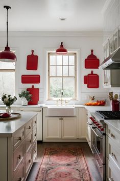 a kitchen with white cabinets and red hanging lights over the stove top, along with an area rug on the floor