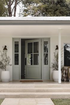 the front door of a white house with potted plants