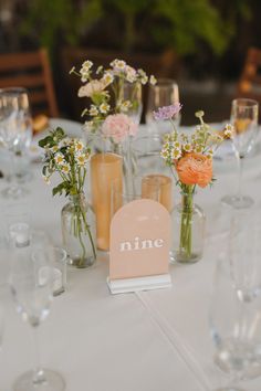 the table is set with wine glasses and vases filled with different types of flowers