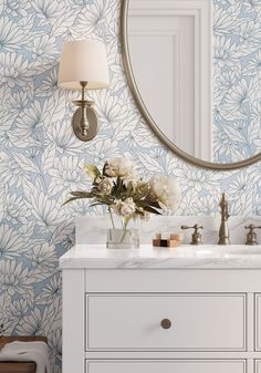 a bathroom with blue and white wallpaper and a round mirror on the wall above it