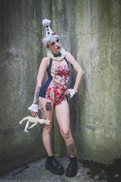 a woman dressed in costume standing next to a cement wall with her hands behind her back