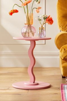 a pink table with vases and flowers on it in front of a yellow chair