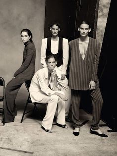 three models pose for a black and white photo in front of a chair with one woman sitting on the other side