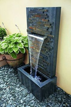 an image of a fountain with water coming out of it and some plants in the background