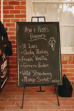 a chalkboard sign sitting on the side of a brick wall next to a window