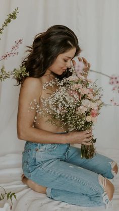 a woman sitting on the ground with flowers in her hand and looking down at her stomach