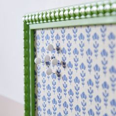 a blue and white wall hanging with three buttons on it's side, attached to a green frame