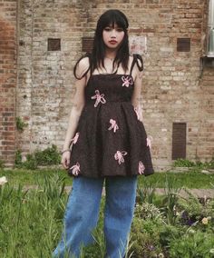 a woman standing in front of a brick building wearing blue jeans and a black top