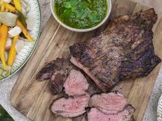 some meat and vegetables on a cutting board next to a bowl of green pesto