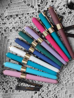 several different colored pens sitting on top of a white lace covered table next to a black purse