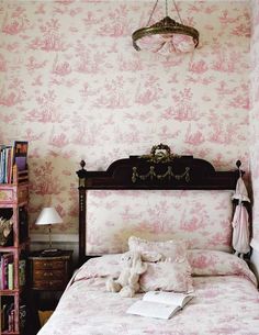 a bed in a bedroom with pink wallpaper and a chandelier above it