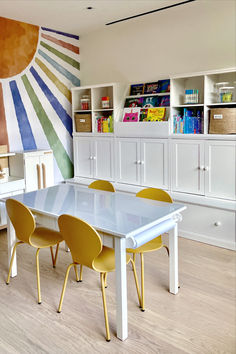 a dining room table with yellow chairs in front of a bookcase and bookshelf