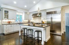 a large kitchen with white cabinets and black counter tops, an island in the middle is flanked by three stools