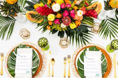 the table is set with place settings and tropical flowers on top of each place setting