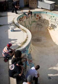 skateboarders are gathered around the edge of an empty pool with graffiti on it