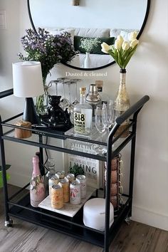 a bar cart with wine glasses and bottles on it in front of a round mirror