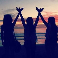 three girls standing on the beach with their arms in the air and one girl holding her hands up