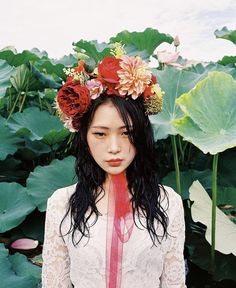 a woman with flowers on her head standing in front of large leaves and water lilies