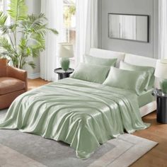 a bed with green sheets and pillows in a living room next to a couch, chair and window