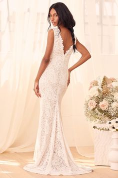 a woman in a white wedding dress standing next to a vase with flowers on it