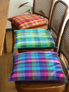 three chairs with colorful cushions on them in front of a wooden table and chair cushion