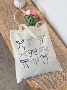 a white bag sitting on top of a wooden table next to a vase filled with flowers