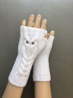 two hands with white knitted gloves on top of each other, one has an owl head