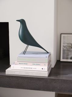 a stack of books with a bird statue on top of them next to two framed pictures