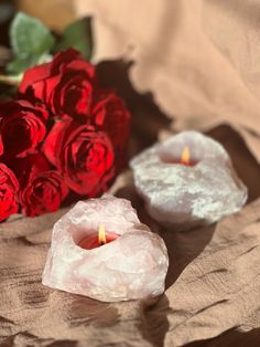 two candles are sitting next to some red roses