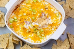 a casserole dish filled with cheese and vegetables surrounded by tortilla chips