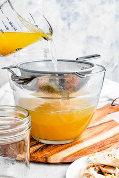 someone pouring orange juice into a bowl on top of a cutting board next to other ingredients