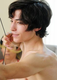 a shirtless young man holding an arrow in his right hand