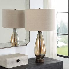 two lamps are sitting on a dresser next to a mirror and a box with a ring in it