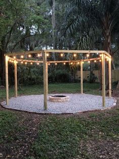 an outdoor fire pit with lights strung around it in the middle of a garden area