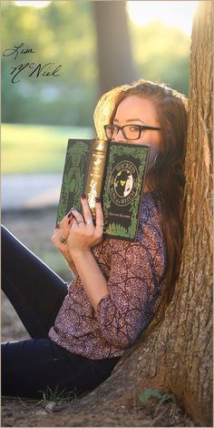 a woman is sitting under a tree and reading a book with her hands on her face