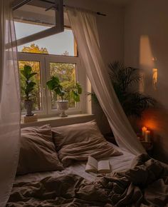 an unmade bed sitting in front of a window with curtains over it and a lit candle