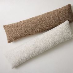 two pillows sitting next to each other on top of a white table with a brown pillow