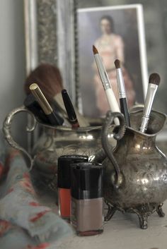 a silver vase filled with makeup brushes and other items next to an image of a woman's face