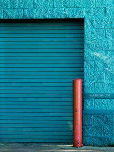 an orange fire hydrant in front of a blue garage door with a red pole