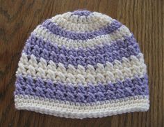 a purple and white crocheted hat sitting on top of a wooden table next to a pair of scissors