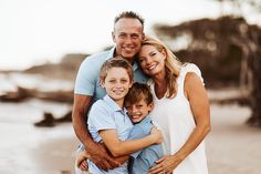 a man, woman and two boys are posing for a photo on the beach with their arms around each other