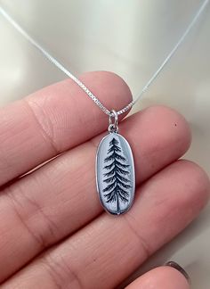 This minimalist Pine Tree Necklace makes the perfect Anniversary, Birthday or Christmas Gift!  Featuring a Solid .925 Sterling Silver 1 inch Pine Tree Oval Pendant and a Solid .925 Sterling Silver Cable or Box Chain. Perfect for everyday wear. Choice of Necklace Gift Box. Add a Birthstone to this Necklace here: https://www.etsy.com/listing/886396220/sterling-silver-tiny-swarovski-crystal?ref=shop_home_active_3&crt=1 Click on Link to Shop our Etsy Store: https://www.etsy.com/shop/LastingMemoryJewelry Pine Cone Jewelry, Pine Jewelry, Tree Jewelry, Wanderlust Jewelry, Forest Pendant, Hiking Jewelry, Nature Jewelry, Mountain Necklace, Mountain Jewelry, Best Seller, Autumn Jewelry, Fall Jewelry, Christmas Jewelry, Christmas Gift, Anniversary Gift, Birthday Gift, Gift for Her, Gifts for girlfrie Hiking Jewelry, Pine Cone Jewelry, Pine Jewelry, Christmas Tree Necklace, Tiny Cross Necklace, Silver Initial Charms, Initial Necklace Silver, Wanderlust Jewelry, Woodland Jewelry