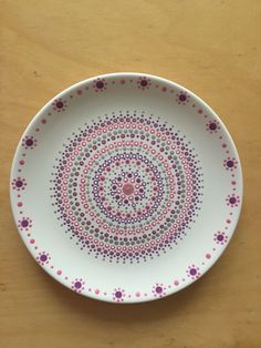 a white plate with pink, purple and green dots on it sitting on a wooden table