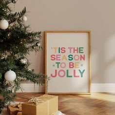 a christmas tree with presents under it in front of a framed holiday card that says tis the season to be jollyy