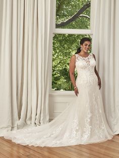 a woman standing in front of a window wearing a wedding dress