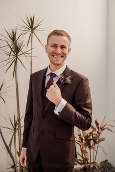 a man in a suit and tie is smiling at the camera while standing next to a potted plant