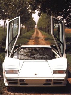 a white sports car parked on the side of a dirt road with its doors open